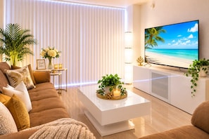 A modern living room with a flat-screen TV, a sofa, a coffee table with decorative items, and a large window with blinds.