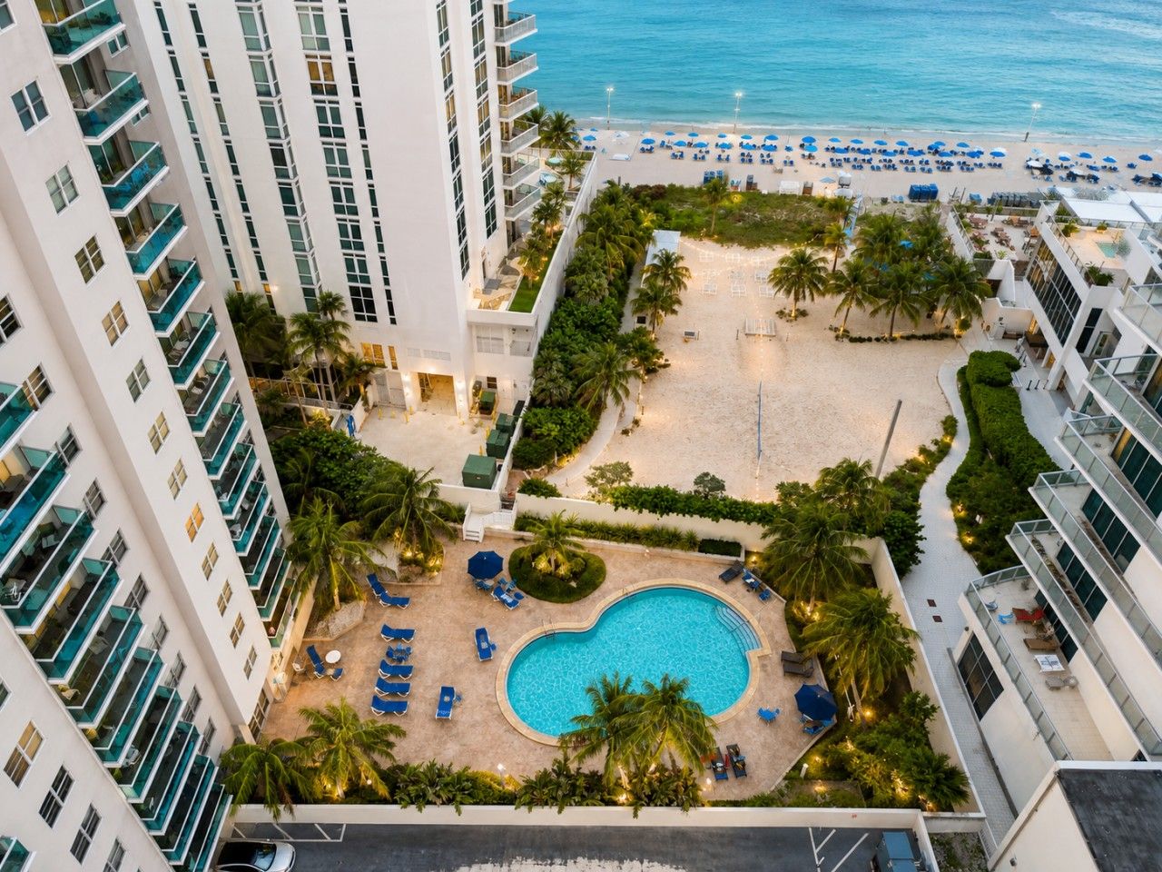 Un hôtel doté d’une piscine entourée de palmiers et de chaises longues, avec vue sur une plage.