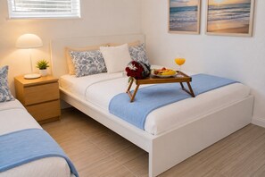 Uma cama de solteiro com mesa de cabeceira, abajur e bandeja com frutas e um copo de suco de laranja.