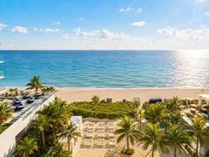 A beach view with a pool area, palm trees, and lounge chairs.