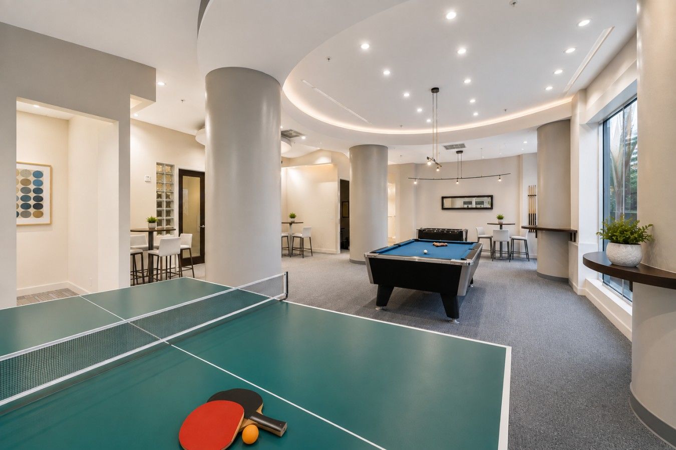 A pool table with a red and black table tennis paddle, a billiards table, and a dining area with chairs and a table.