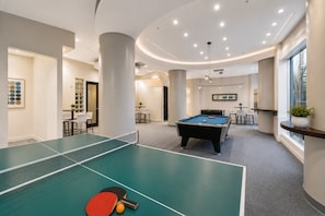 A pool table with a red and black table tennis paddle, a billiards table, and a dining area with chairs and a table.