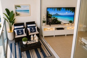 A living room with a television, two chairs with nautical pillows, a coffee table with a 'Beach' sign, and a potted plant. - Hollywood Oceanfront Condo| Ocean+ Pool Views| Sleeps 6| Game Room (Hollywood)