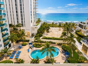 A resort with a pool surrounded by palm trees and lounge chairs, overlooking a beach.