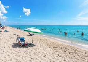 Uma praia com águas azul-claras, pessoas nadando e cadeiras de praia com guarda-sóis.