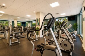 Uma academia com equipamentos de cardio, máquinas de musculação e espelhos.