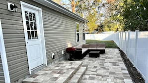 A patio with a stone-tiled floor, a white door, and a brown outdoor seating area. - Snow Birds Welcome. 10 min to Downtown & Beach (St. Augustine)