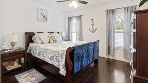 A bedroom with a bed, a nightstand, a ceiling fan, a window with curtains, and a wall-mounted anchor decoration. - Snow Birds Welcome. 10 min to Downtown & Beach (St. Augustine)