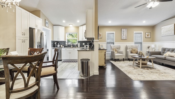A spacious living area with a dining table and chairs, a kitchen in the background, and a ceiling fan. - Snow Birds Welcome. 10 min to Downtown & Beach (St. Augustine)