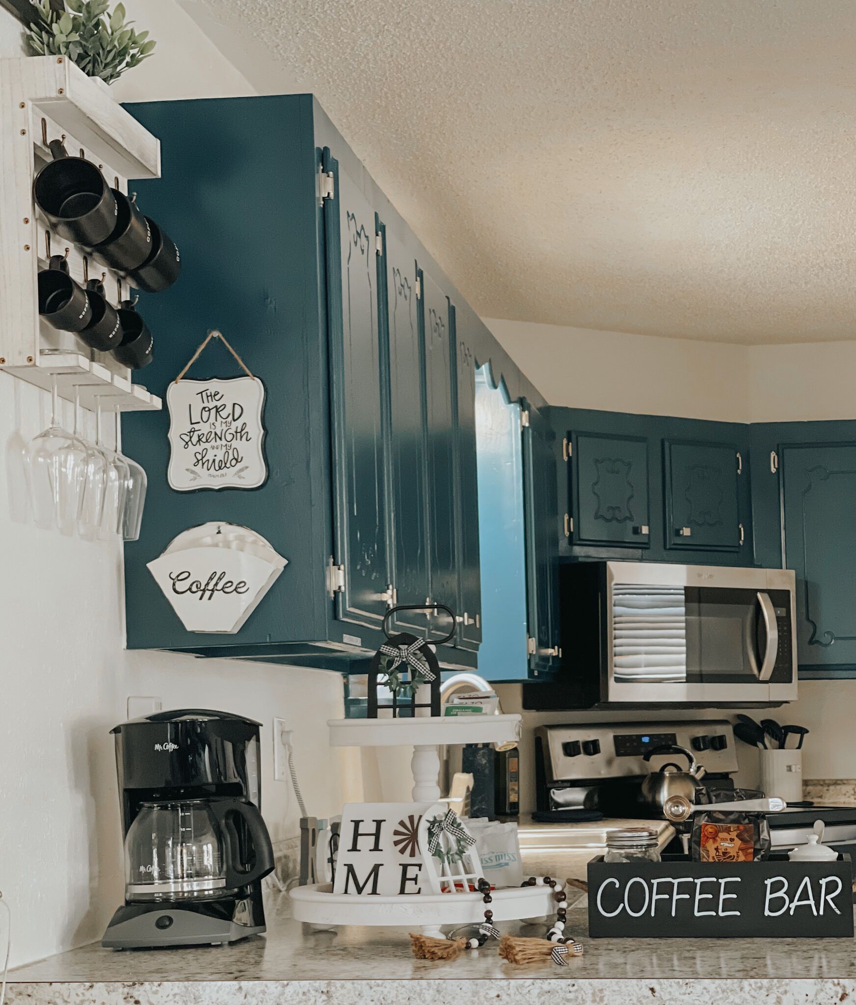 A kitchen with teal cabinets, a coffee maker, a microwave, and a coffee bar sign.