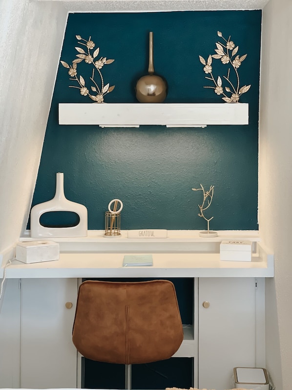 A desk with a teal wall, a white shelf, and a brown chair.