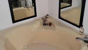 Un baño con una bañera grande, dos espejos y un pequeño adorno en el borde de la bañera.