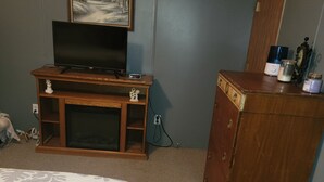 Un dormitorio con cama, cómoda de madera, televisor sobre un mueble bajo y un cuadro en la pared.