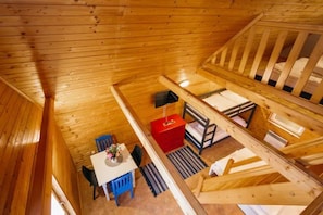 A wooden cabin with a dining area, a red chest of drawers, and a staircase.