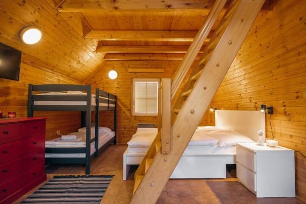 A wooden cabin bedroom with bunk beds, a red dresser, and a staircase.