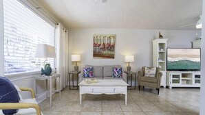 A living room with a sofa, a coffee table, a TV, and a painting of flamingos. - Blue Ocean ~ Pet Friendly ~ One house off the Beach! (Saint Augustine)