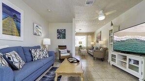 A spacious living room with a blue sofa, a wooden coffee table, and a television on a white cabinet. - Blue Ocean ~ Pet Friendly ~ One house off the Beach! (Saint Augustine)