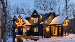 Una casa grande de madera oscura con varias ventanas y un balcón, rodeada de nieve.