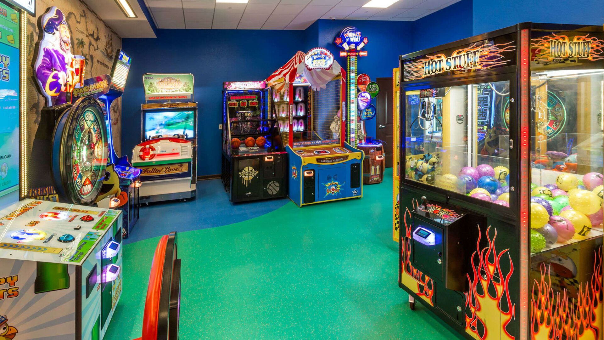 Eine Indoor-Spielhalle mit verschiedenen Spielautomaten, darunter ein Pac-Man-Automaten, eine Kegelbahn und Greifklauen-Spielautomaten.