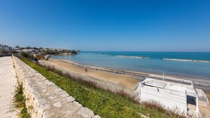 Blick auf die Küste mit einer Steinmauer, einem Strand und einem kleinen Gebäude mit Metallbedachung.