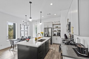 Een moderne keuken met een centraal eiland, roestvrijstalen apparatuur en hangende lampen.