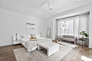 Ein modernes Schlafzimmer mit Bett, Nachttischen, einer Bank, einem Sofa und einem Fenster mit Vorhängen.