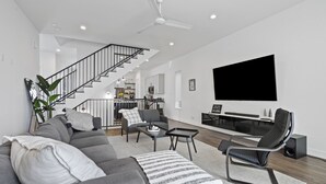 A modern living room with a grey sofa, a black leather chair, a coffee table, and a TV mounted on the wall. - Modern Townhome near Galleria - Garage Gym / Private Backyard (Houston)