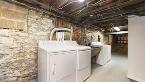 Une buanderie avec des lave-linge et des sèche-linge superposés, des murs en pierre, des conduits apparents et un sol en béton.