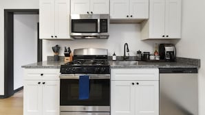 Une cuisine moderne avec des meubles blancs, une cuisinière en acier inoxydable, un four à micro-ondes et une machine à café.