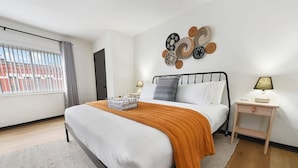 Une chambre à coucher moderne avec un lit, une table de chevet, une lampe et une œuvre d’art murale.