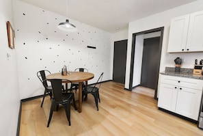A modern kitchen with white cabinets, a wooden dining table with chairs, and a hanging light fixture. - ★ HostWise Stays ★ Off Street Parking, Central Lawrenceville, Butler St. Apartment! (Pittsburgh)