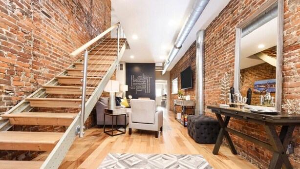 Een moderne loft met blootgelegde bakstenen muren, een houten trap, een eethoek met een grote spiegel en een gezellige zithoek.
