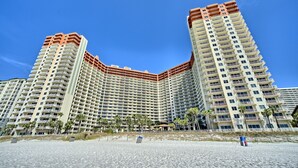 A large, multi-story hotel with a curved facade, located near a sandy beach.