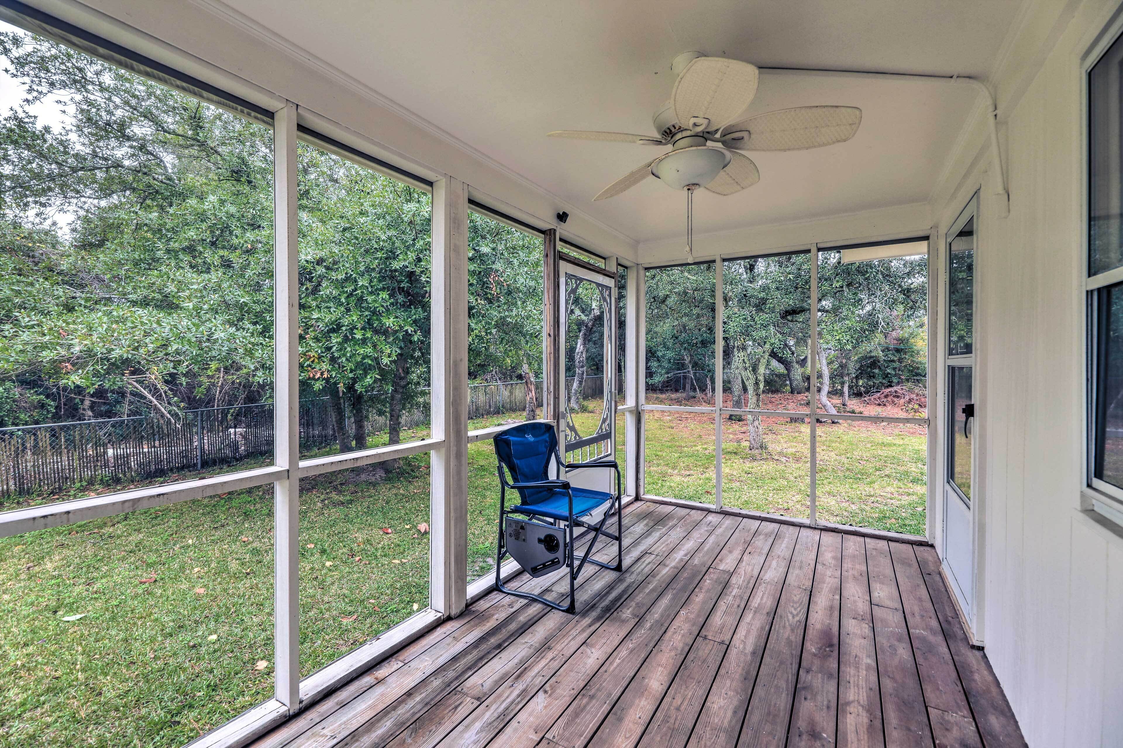 A covered porch with a ceiling fan, large windows, and a blue chair.