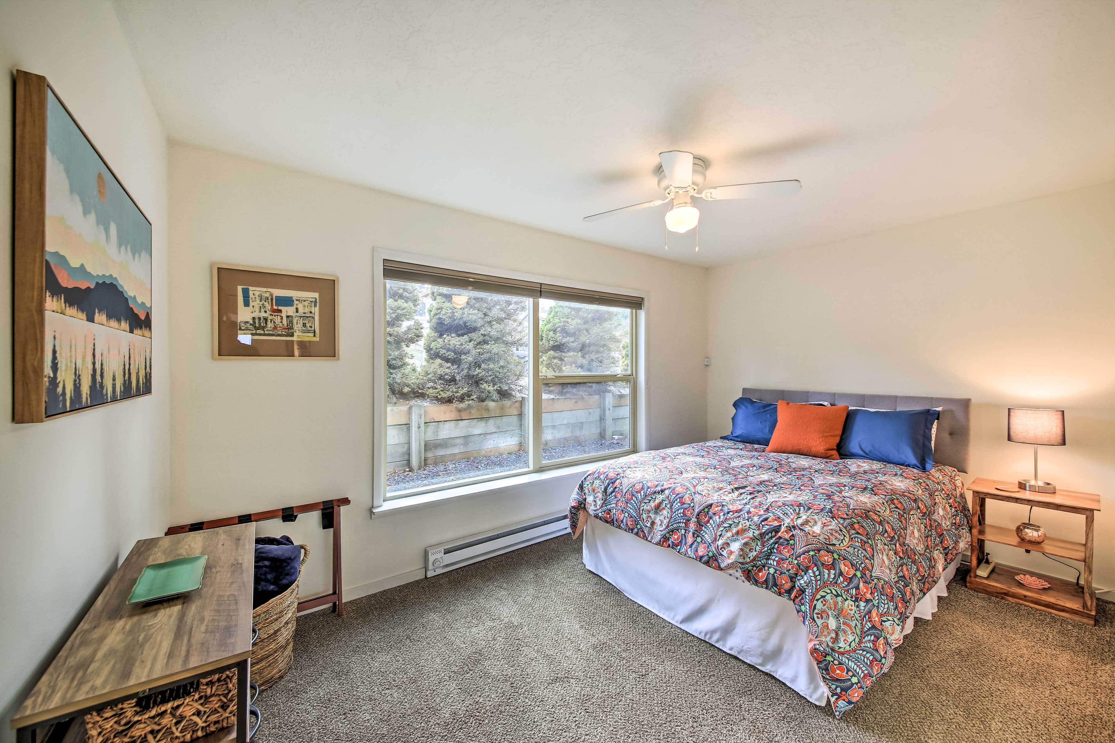 A bedroom with a bed, a desk, a chair, a window, and a ceiling fan.