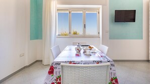 Ein Essbereich mit einem Tisch für zwei Personen, einem Fenster mit Vorhängen und einem Flachbildfernseher an der Wand.