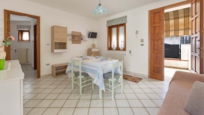 Un coin repas avec une table dressée pour quatre personnes, un téléviseur fixé au mur et une fenêtre avec des rideaux.