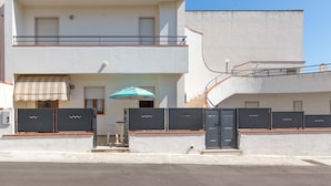 Un bâtiment à deux étages doté d’un balcon, d’un espace extérieur couvert aménagé en coin salon et d’un escalier.