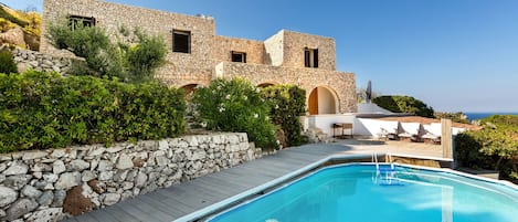 A stone building with a swimming pool, outdoor seating, and a view of the sea.