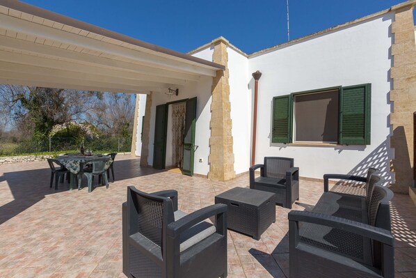 An outdoor patio with a covered seating area, stone walls, and a view of the surrounding landscape.