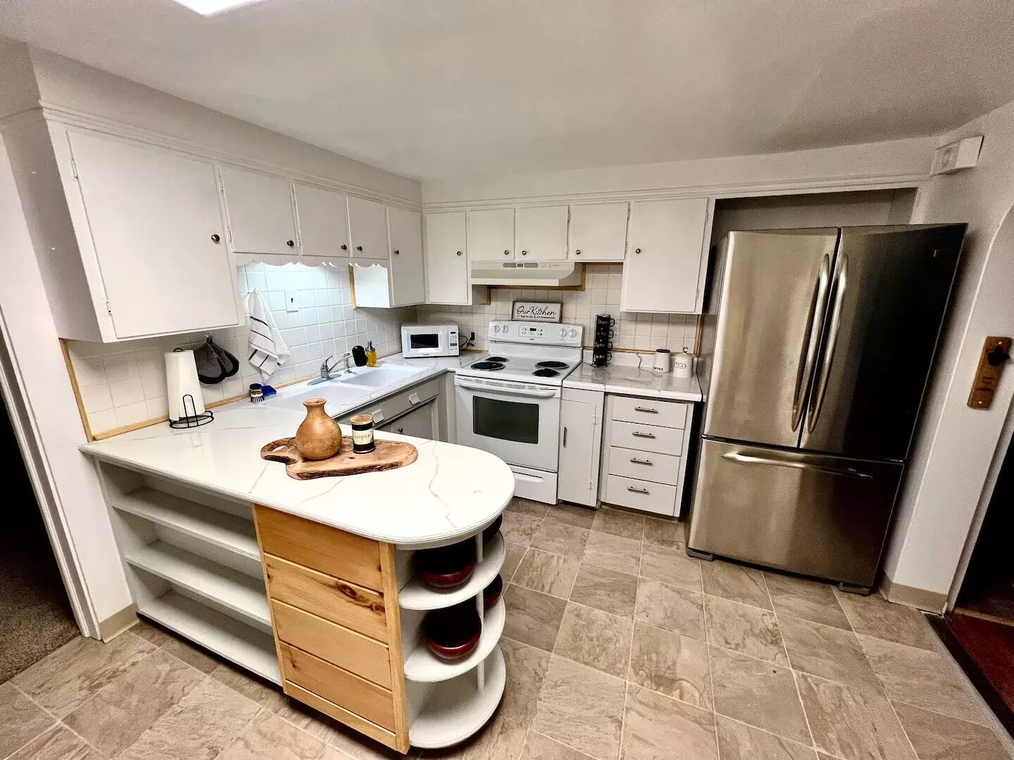 A modern kitchen with white cabinetry, a central island with a wooden base, a stainless steel refrigerator, and a microwave.