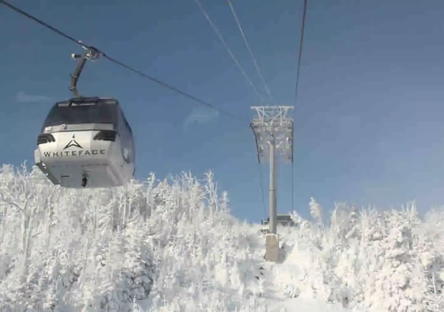 A cable car labeled "WHITEFACE" moving along a cable above a snowy landscape.