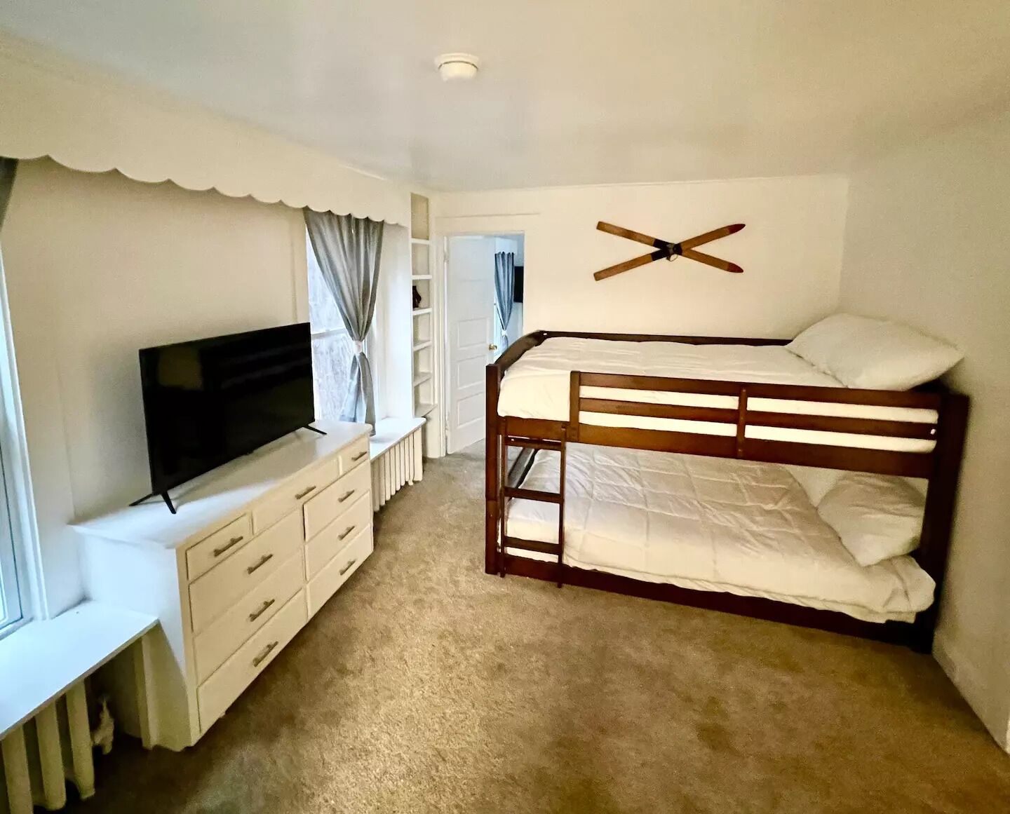 Un dormitorio con literas, televisión, cómoda y radiador.