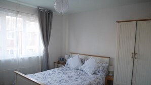 A bedroom with a bed, a nightstand, a wardrobe, and a window with curtains. - Cliffwalk Cottage (Portland)