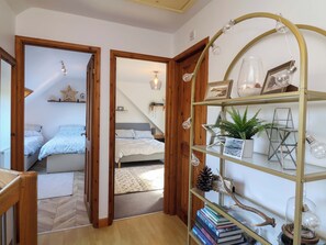 A bedroom with a bed, bedside tables, a wooden door, and a hallway leading to another room.