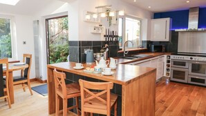 Een moderne keuken met houten vloeren, een centraal eiland met barstoelen, een ingebouwde oven en een groot raam dat voor natuurlijk licht zorgt.