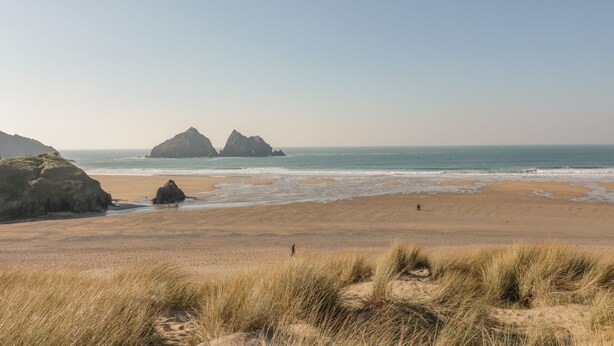Ein Strand mit Dünen und felsigen Formationen im Hintergrund.