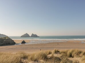 A beach with sand dunes and rocky formations in the distance. - Palm View (Newquay)