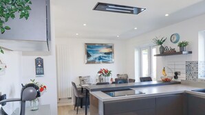 Eine moderne Küche mit einer zentralen Kochinsel, einem Essbereich mit Stühlen, einer Kaffeemaschine und einem Bild an der Wand.