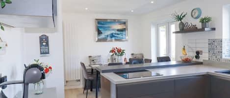 A modern kitchen with a central island, a dining area with chairs, a coffee machine, and a painting on the wall.